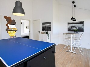 A room with a ping pong table, white furniture, and a cityscape painting.