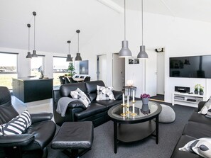 A modern living room with a black leather sofa, a glass coffee table, and pendant lighting.