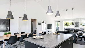 Une cuisine moderne dotée d’un grand îlot central, de luminaires suspendus et d’un coin repas avec une table et des chaises en bois.
