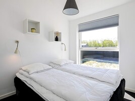 Un dormitorio con cama, mesitas de noche, una ventana con persianas y una lámpara colgante.