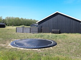 Un trampolín en un área con césped y un edificio negro al fondo.
