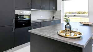 Une cuisine moderne avec des meubles de couleur sombre, un four encastré, un évier en acier inoxydable et des luminaires suspendus.
