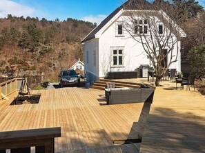 Ein weißes Haus mit Holzterrasse, Sitzgelegenheiten im Freien und Grillplatz.