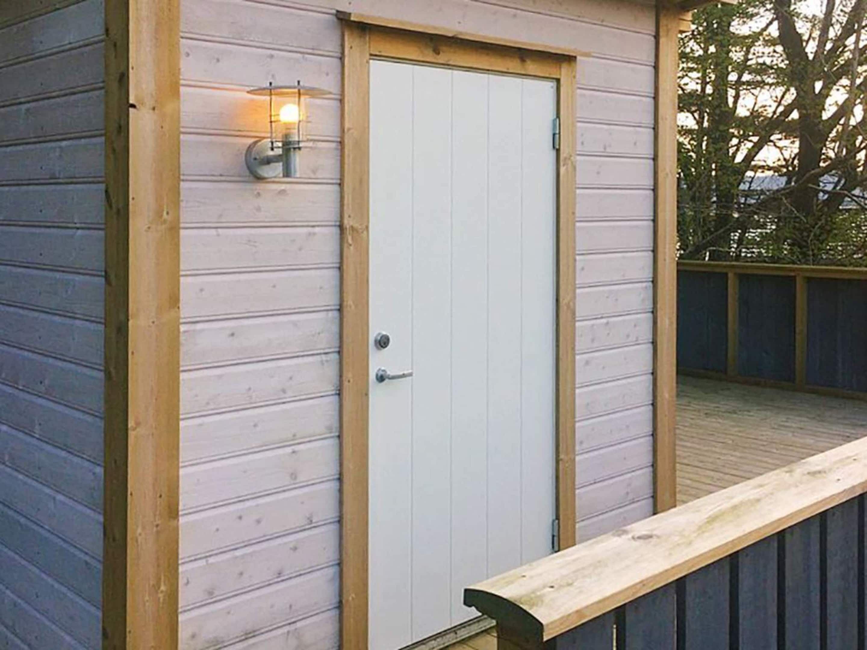 Una cabana de fusta amb una porta blanca, un petit porxo i un llum penjada a la paret.