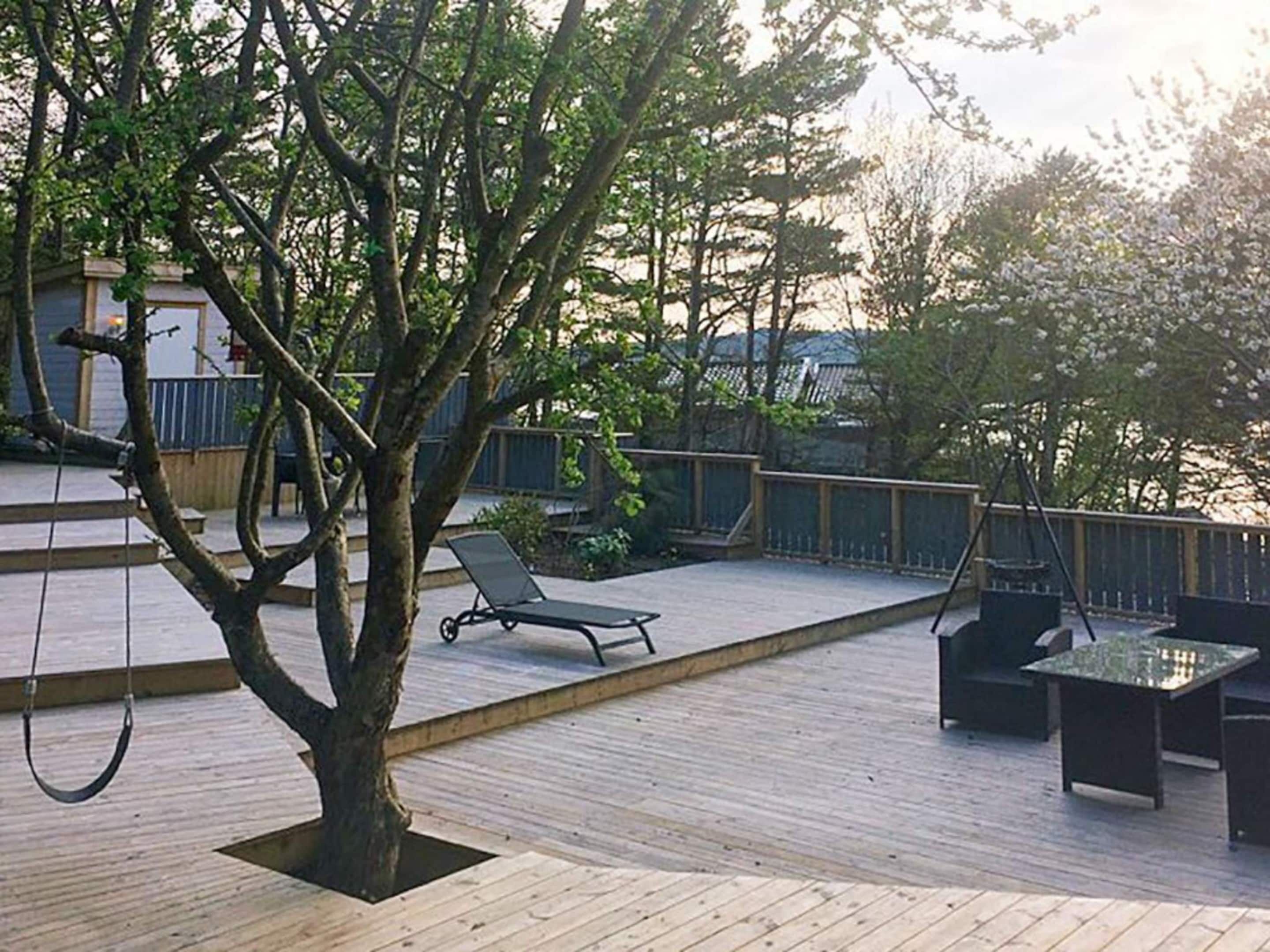 A wooden deck with a swing, a lounge chair, and a small table.