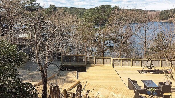 Eine Holzterrasse mit Gartenmöbeln, mit Blick auf einen See, umgeben von Bäumen.