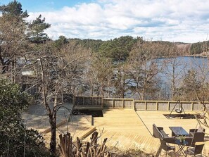 Una terraza de madera con mobiliario exterior, con vista a un lago rodeado de árboles.