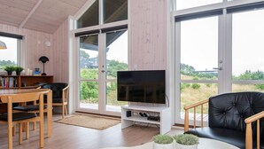 Una sala de estar moderna con televisor, muebles de madera y ventanas amplias.