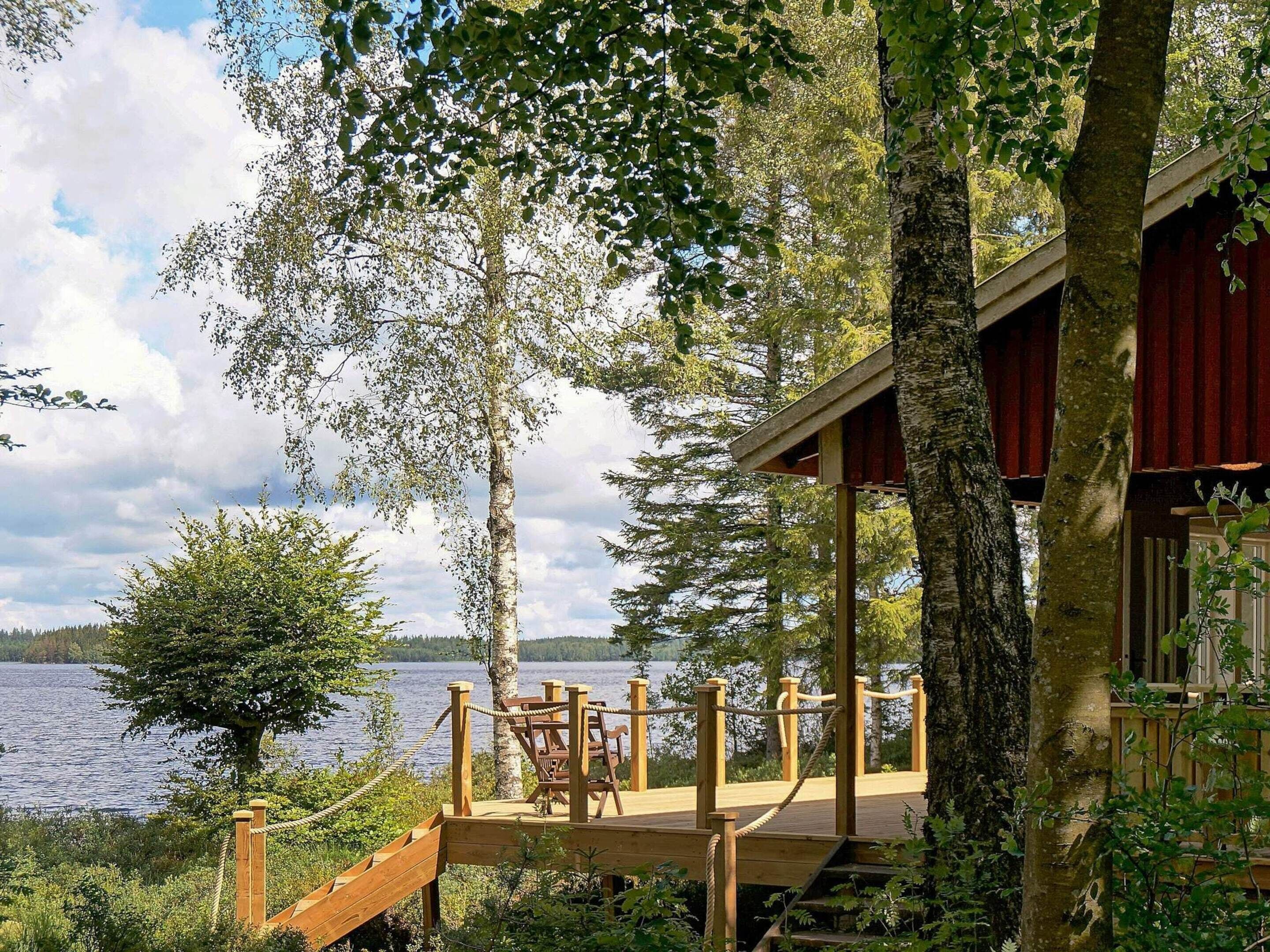 Une terrasse en bois, agrémentée de chaises, qui offre une vue sur un lac et est entourée d’arbres.