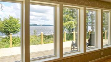 A room with large windows overlooking a lake and a deck area with a chair.