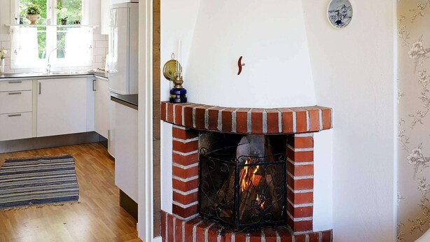 A kitchen with a brick fireplace, wooden flooring, and a window with plants. - 8 Person Holiday Home in Hyltebruk (Hyltebruk)