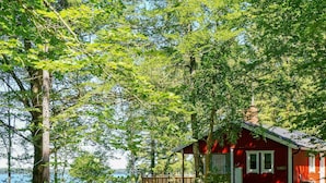 A red cabin with a porch, surrounded by lush greenery and a lake view. - 8 Person Holiday Home in Hyltebruk (Hyltebruk)