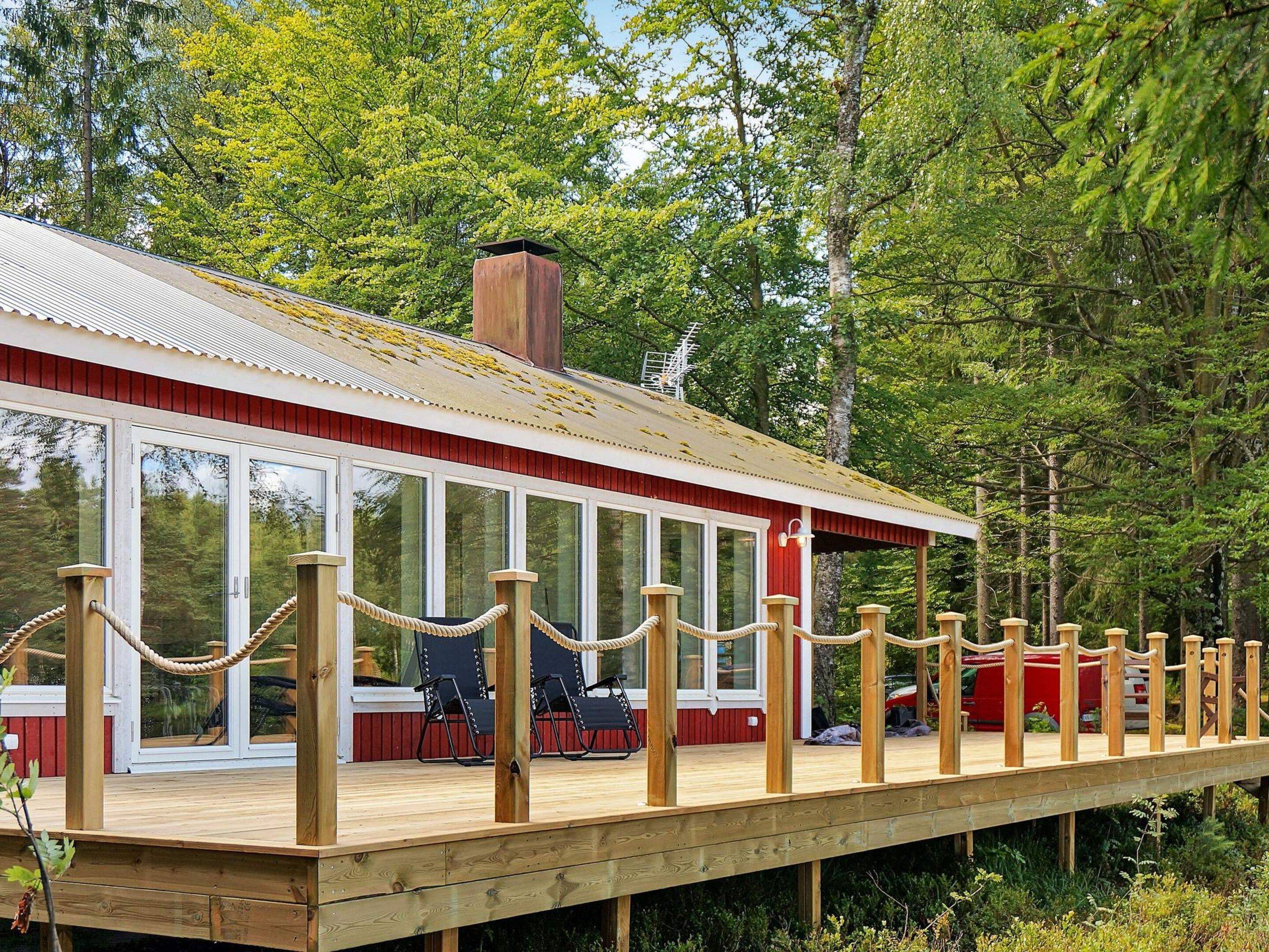 A wooden deck with a railing, a red building with large windows, and a forested background.