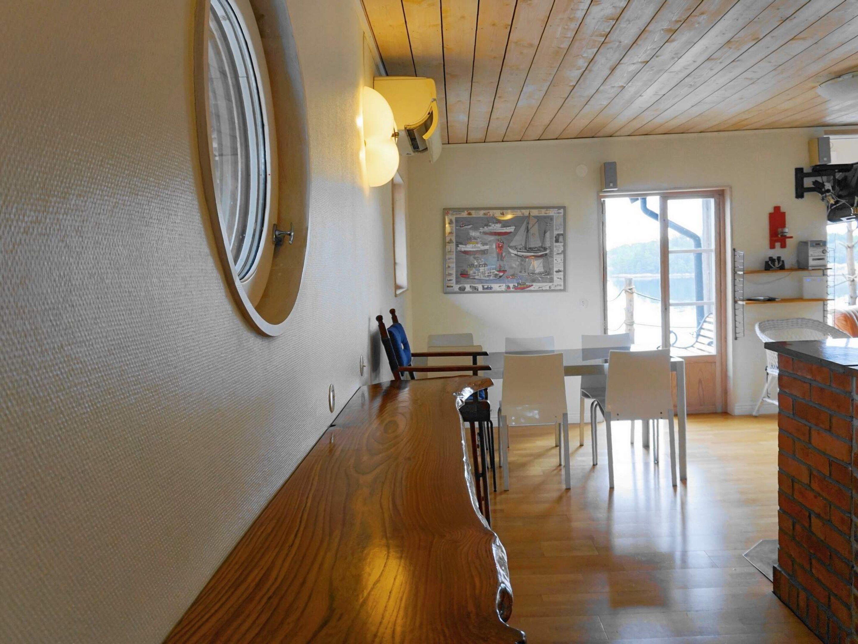 A room with a wooden floor, a round mirror, a dining area with chairs and a table, and a view through a window.