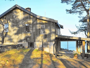 A rustic wooden house with a stone foundation, a covered entryway, and a view of the water.