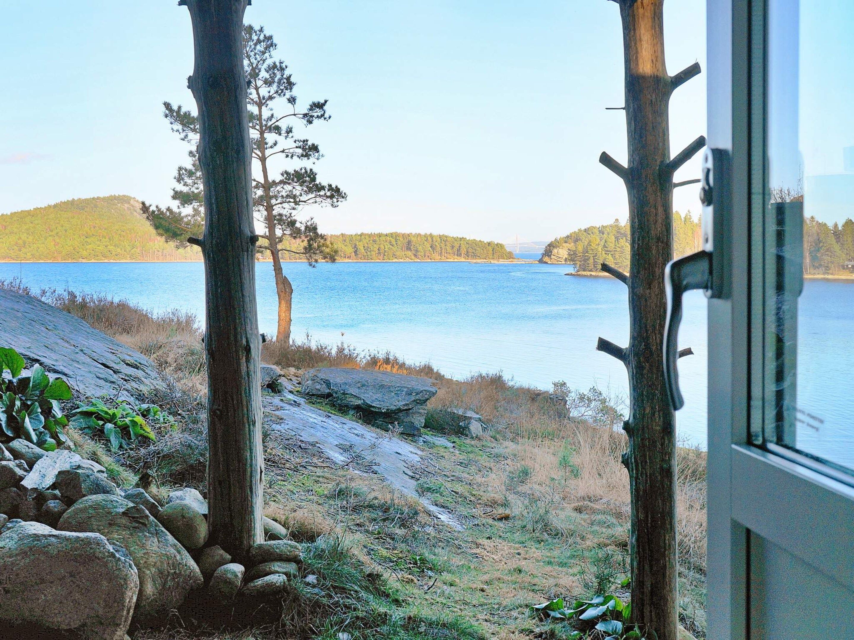 A view from a window overlooking a lake with trees and a distant bridge.