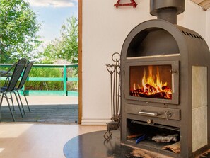 A wood-burning stove with a fire burning inside, a metal chair, and a green fence in the background. - 6 Person Holiday Home in Skibby (Skibby)