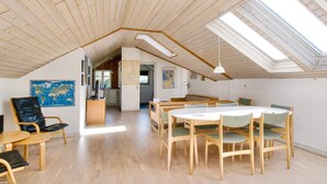 A spacious loft with a high ceiling, wooden beams, a skylight, a dining area with a round table and chairs, a kitchen in the background, and a large world map on the wall. - 6 Person Holiday Home in Skibby (Skibby)