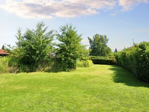 A well-maintained grassy area with trees and shrubs, a clear sky, and a building with a red roof in the background. - 6 Person Holiday Home in Skibby (Skibby)