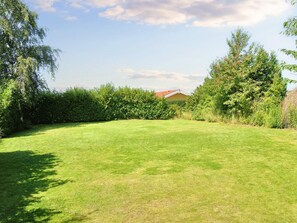 A well-maintained grassy yard with a hedge and trees, a house in the background, and a clear sky. - 6 Person Holiday Home in Skibby (Skibby)