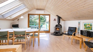 A cozy room with a high ceiling, wooden beams, a central fireplace, and a large window overlooking greenery. - 6 Person Holiday Home in Skibby (Skibby)
