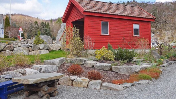 A red wooden cabin with a sloped roof, surrounded by a stone wall and a gravel path. - 8 Person Holiday Home in Skiftun (Hjelmeland)