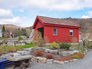 Una cabaña de madera roja con techo inclinado, rodeada por un muro de piedra y un sendero de grava.