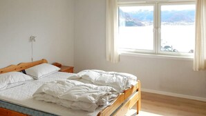 A single bed with a wooden frame, white bedding, and a view of a lake and mountains through a window. - 8 Person Holiday Home in Skiftun (Hjelmeland)