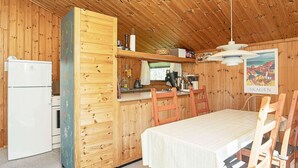 A compact kitchen with wooden walls, a white refrigerator, a dining table with chairs, and a hanging light fixture. - Vintage Holiday Home in Jutland near Child Friendly Beach (Aalbaek)