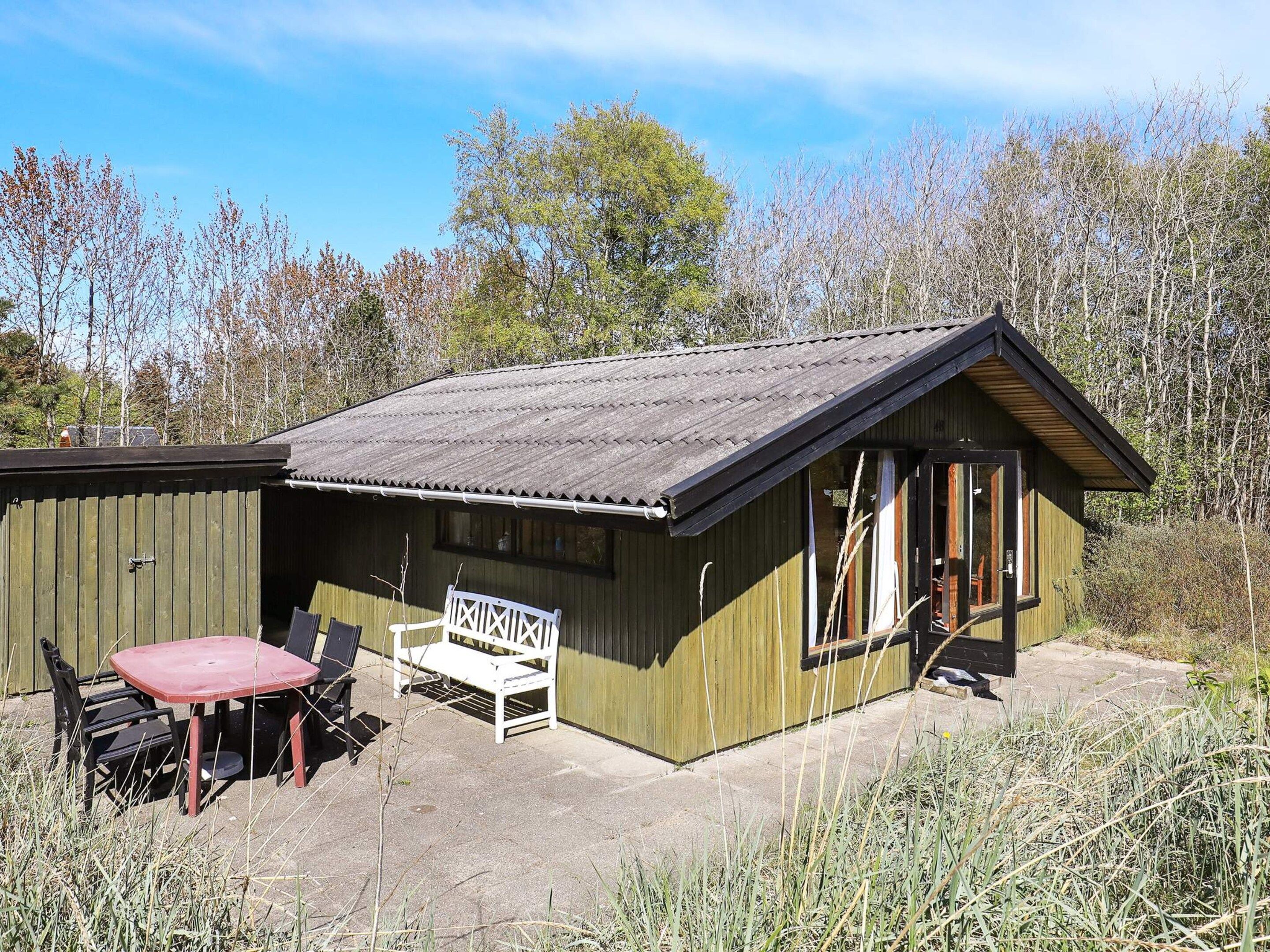 A wooden cabin with a metal roof, a patio with a table and chairs, and a bench.