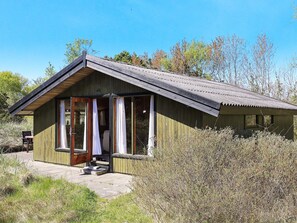 Une petite cabane en bois à un seul étage, avec un toit en pente, une porte d’entrée et un petit porche.