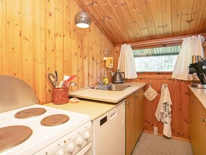 Une cuisine de taille réduite avec des murs en bois, une cuisinière, un évier et une fenêtre avec des rideaux.