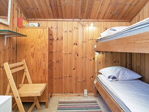 A wooden bunk bed room with a desk and chair, a striped rug, and a small shelf with items.