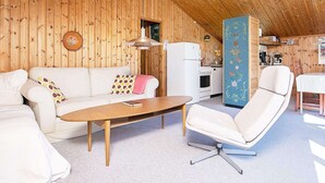 A cozy room with a wooden ceiling, a white sofa, a wooden coffee table, a white armchair, and a kitchen area with a white refrigerator and stove. - Vintage Holiday Home in Jutland near Child Friendly Beach (Aalbaek)