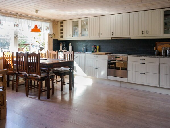 A kitchen with wooden cabinets, a dining table with chairs, and a window with curtains. - 4 Person Holiday Home in Ormaryd (Ormaryd)