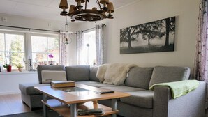 A modern living room with a grey sofa, a wooden coffee table, and a painting of trees on the wall. - 4 Person Holiday Home in Ormaryd (Ormaryd)