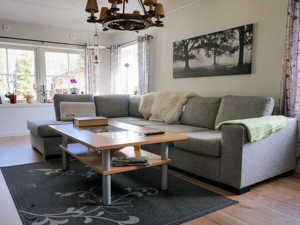 A modern living room with a grey sofa, a wooden coffee table, and a painting of trees on the wall. - 4 Person Holiday Home in Ormaryd (Ormaryd)