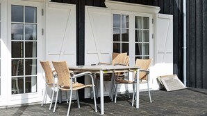 A covered patio with a table and chairs, white doors, and a wooden deck. - 4 Star Holiday Home in Gjern (Gjern)