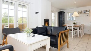 A cozy living room with a black leather sofa, a white coffee table, and a fireplace. There is a dining area with a white table and chairs. - 4 Star Holiday Home in Gjern (Gjern)