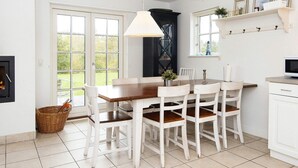 A kitchen with a dining table, chairs, a hanging light fixture, a fireplace, and a window with a view of greenery. - 4 Star Holiday Home in Gjern (Gjern)