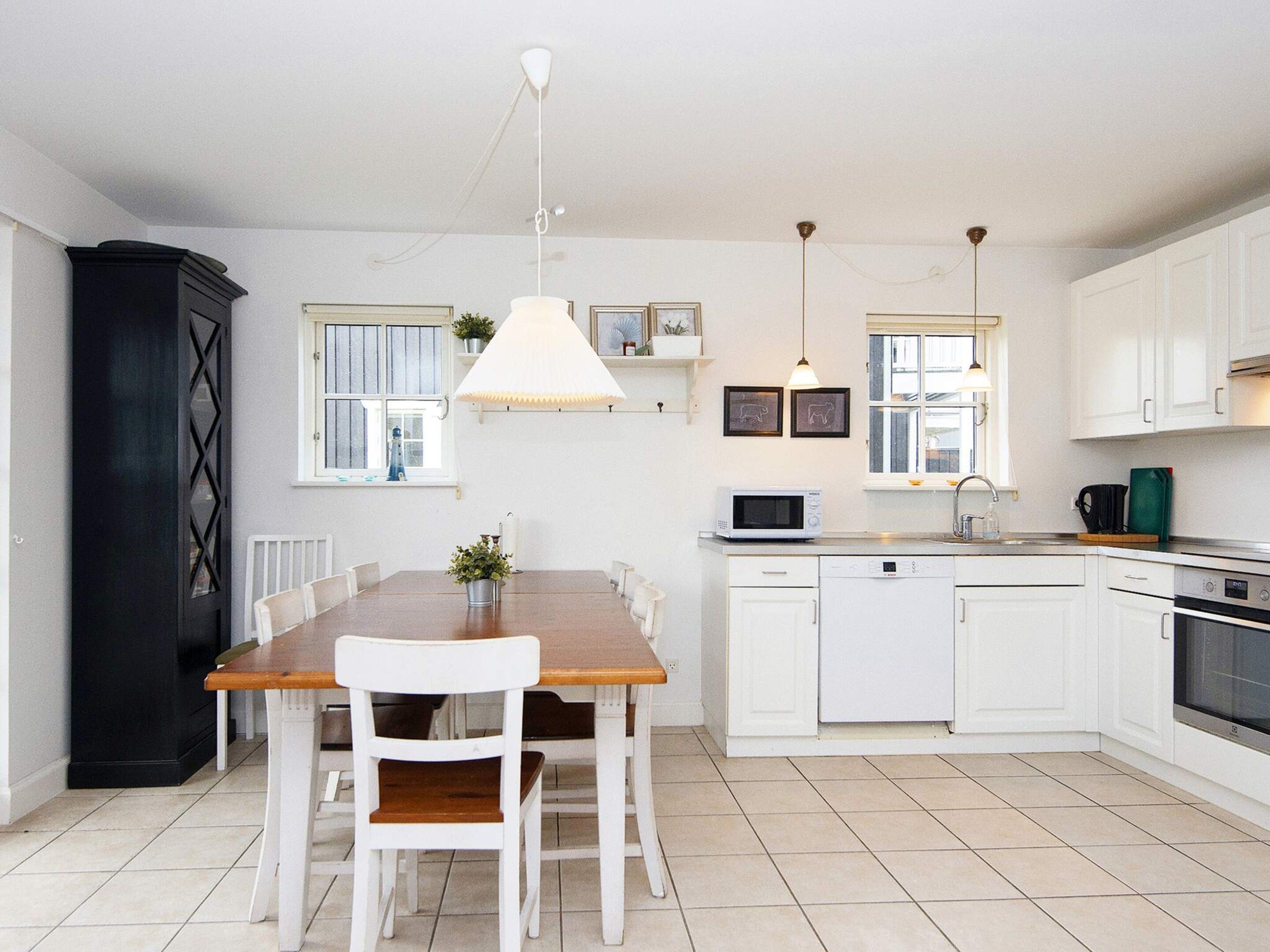 A modern kitchen with white cabinets, a wooden dining table, and a black cabinet.