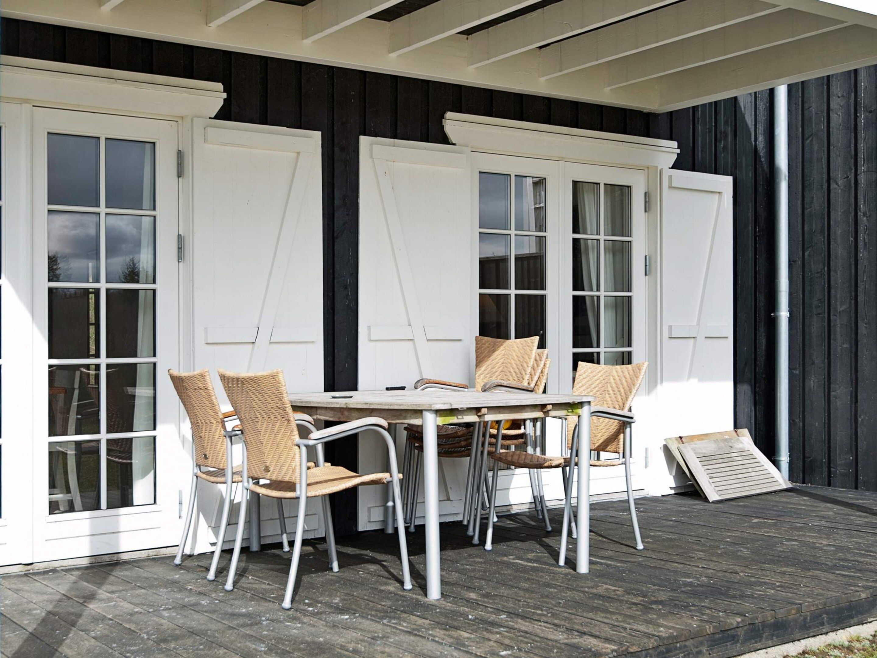 A covered outdoor seating area with a table and chairs, white doors with glass panels, and a wooden deck.