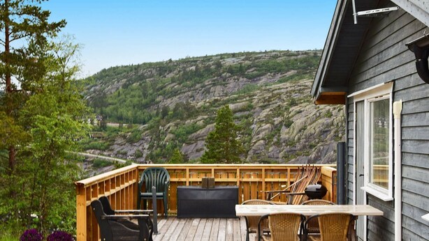 Un patio in legno con mobili da esterno, un'ampia finestra e vista su un pendio roccioso.