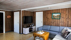 Un soggiorno con pavimento in legno, un divano grigio, un tavolino da caffè in legno e una televisione su una parete in legno.