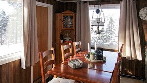 Una sala da pranzo in legno con un tavolo grande, quattro sedie, un lampadario e un mobile contenitore in legno con vetrate.