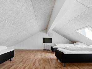 A modern attic bedroom with a sloped ceiling, wooden flooring, and two beds.