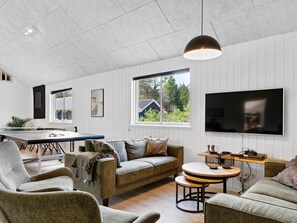 A modern living room with a sofa, chairs, a dining table, and a TV mounted on the wall.