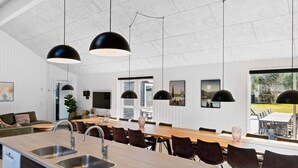 Uma cozinha moderna com ilha central, pias de aço inoxidável e luminárias pendentes pretas.