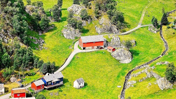 Vista aérea de uma propriedade rural com um celeiro, uma casa pequena e uma área cercada.
