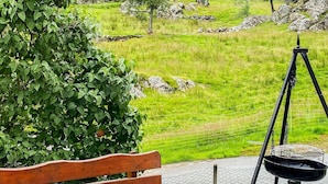 Um banco de madeira e um conjunto de churrasqueira montados numa área pavimentada, com vista para um campo verde e terreno rochoso.